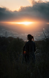 Rear view of man sitting on land against sky during sunset