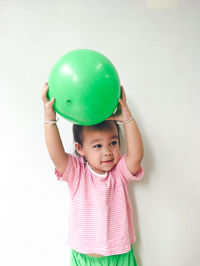 Cute girl holding ball while standing against wall