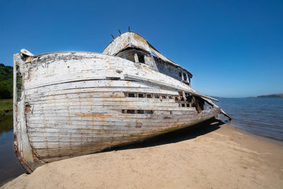 Abandoned boat moored on beach against clear sky