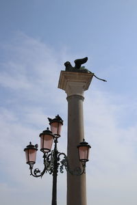 Low angle view of bird perching on street light against sky