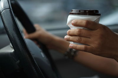 Close-up of hand holding disposable cup while driving car