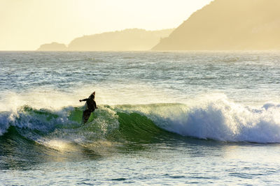 Silhouette man surfing in sea against sky