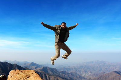 Man jumping on mountain against blue sky