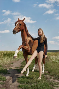 Full length of young woman standing with horse on filed against sky