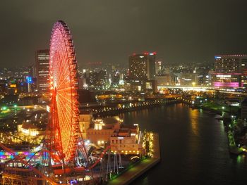 Illuminated cosmo clock 21 by river against buildings in city