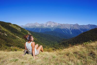 Woman sitting on mountain against clear blue sky