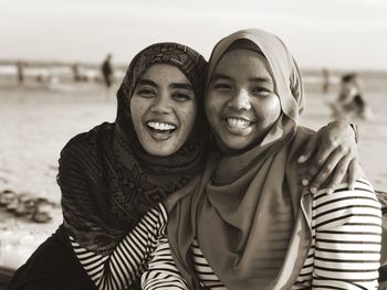 Close-up portrait of smiling friends wearing hijab at beach