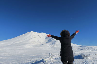 Rear view of person standing on snowcapped mountain against blue sky