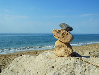 Stacked stones at beach against blue sky