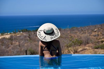 Rear view of woman relaxing in infinity pool against clear sky during sunny day
