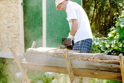 A man in shorts and a panama saws a tree with a chainsaw in his hands