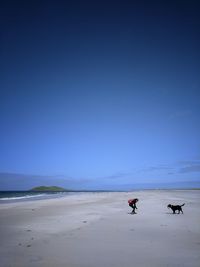 Woman with dog at beach against clear blue sky