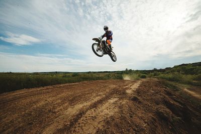 Man with motorcycle jumping on landscape against sky