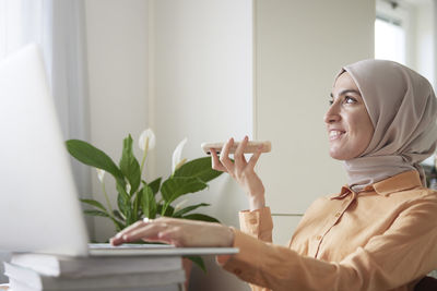 Smiling woman with hijab having conversation on speaker mode on her cell phone