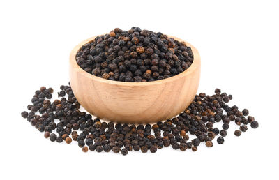 Black peppercorns in bowl against white background