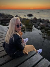 Portrait of young woman sitting at beach during sunset