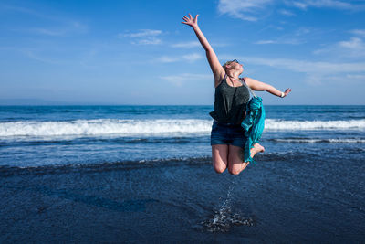 Full length of mature woman jumping on shore at beach against sky