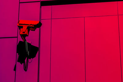 Low angle view of security camera against pink wall