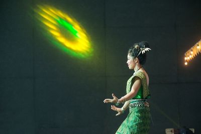 Side view of woman standing against illuminated lighting equipment