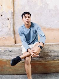 Portrait of young man sitting against wall