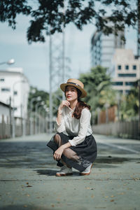 Portrait of young woman crouching on road in city