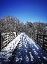 Snow covered footbridge against clear blue sky