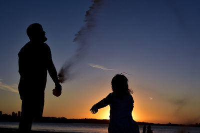 Silhouette couple standing on beach against sky during sunset