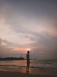 Rear view of man standing on beach during sunset