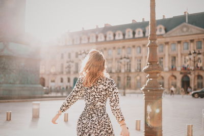 Rear view of woman with arms outstretched against buildings