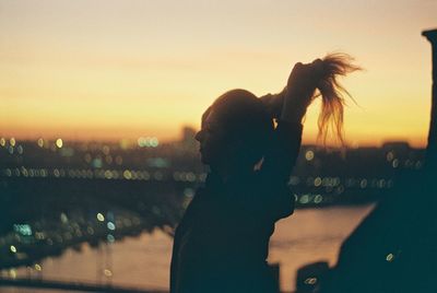 Young woman tying hair while standing against sky during sunset