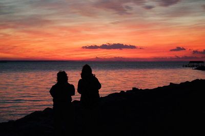 Silhouette of people sitting on beach at sunset