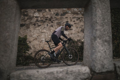 Cyclist riding bicycle in front of stone wall