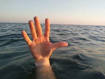 Cropped hand of man in sea against sky