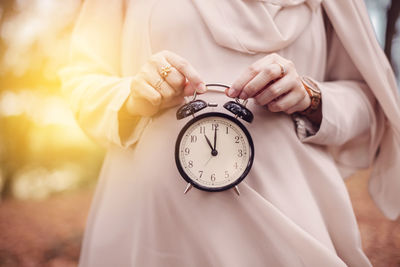Midsection of pregnant woman holding alarm clock
