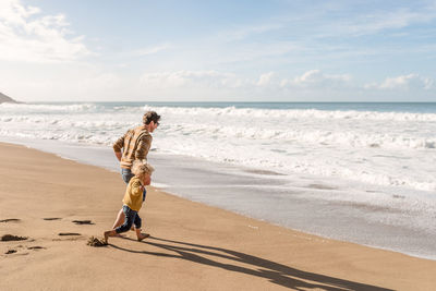 Father and toddler child holding hands and running to wave at a beach