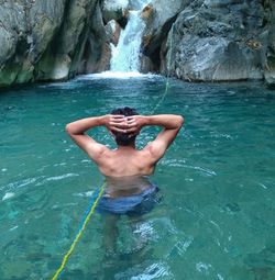 Rear view of shirtless man swimming in river