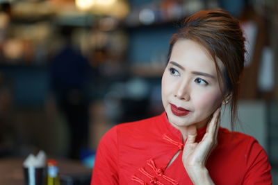 Close-up of thoughtful mature woman wearing red dress sitting indoors