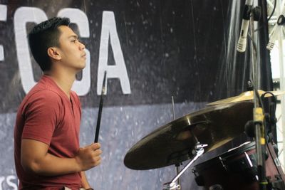 Side view of young man playing drum set on stage