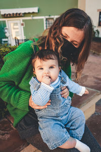 Mother wearing mask with son sitting outdoors