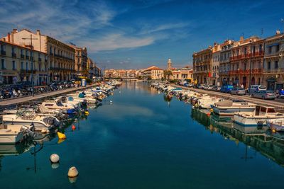 Boats moored in canal amidst buildings in city against sky