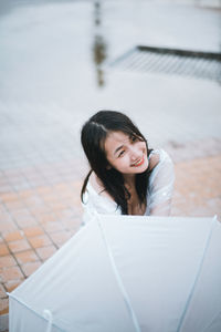 Smiling young woman with umbrella sitting outdoors