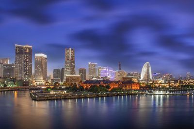 Illuminated city by river against sky