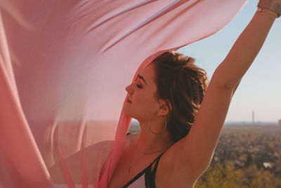 Young woman with pink scarf standing against sky during sunset