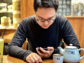 Young man using mobile phone while drinking chinese tea.