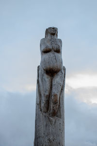 Low angle view of statue on wooden post against sky