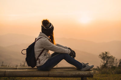 Side view of woman sitting outdoors against sky during sunset