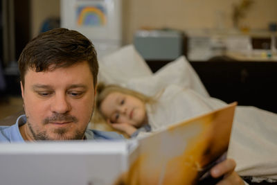 Dad entertains the child during illness. he looks, reads a book, a photo book with his daughter home