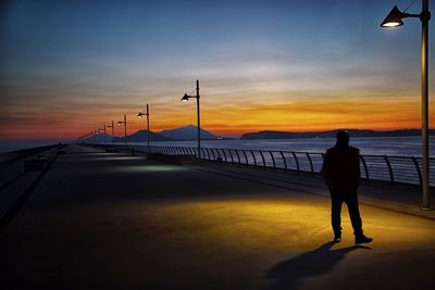 Rear view of silhouette man walking on shore against sunset sky