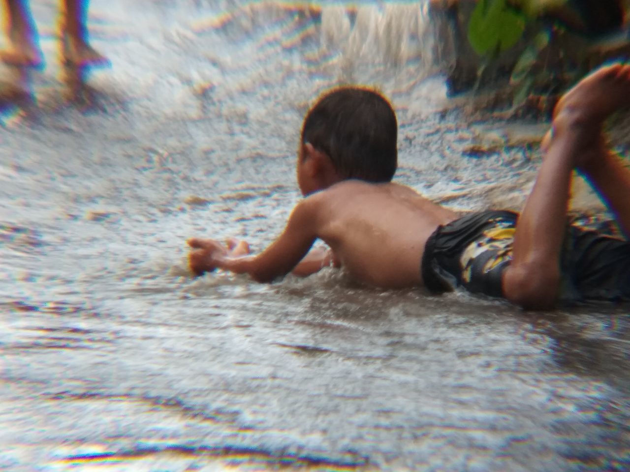 REAR VIEW OF SHIRTLESS BOY IN WATER AT SWIMMING POOL