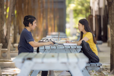 At the public park, a happy young couple using a laptop sits at a table.